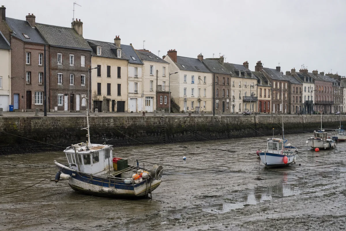 Rangée de maisons de pêcheurs le long d&rsquo;un quai normand à marée basse, ciel gris